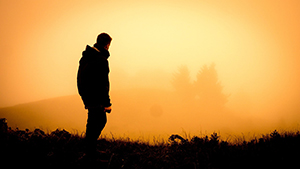 Man hiking silhouetted against an orange sky