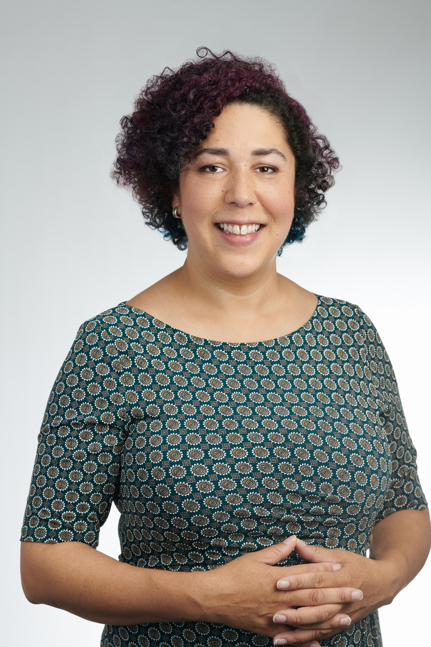 Image of woman standing with crossed hands wearing green print dress. 