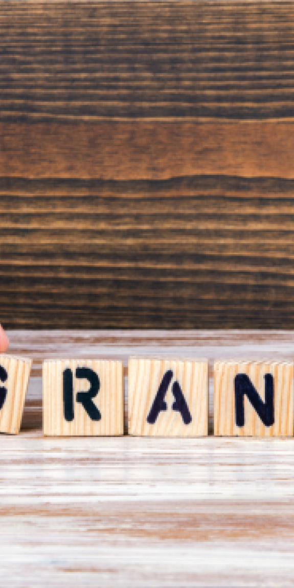 A person's hand arranging blocks to spell out the word "Grant"