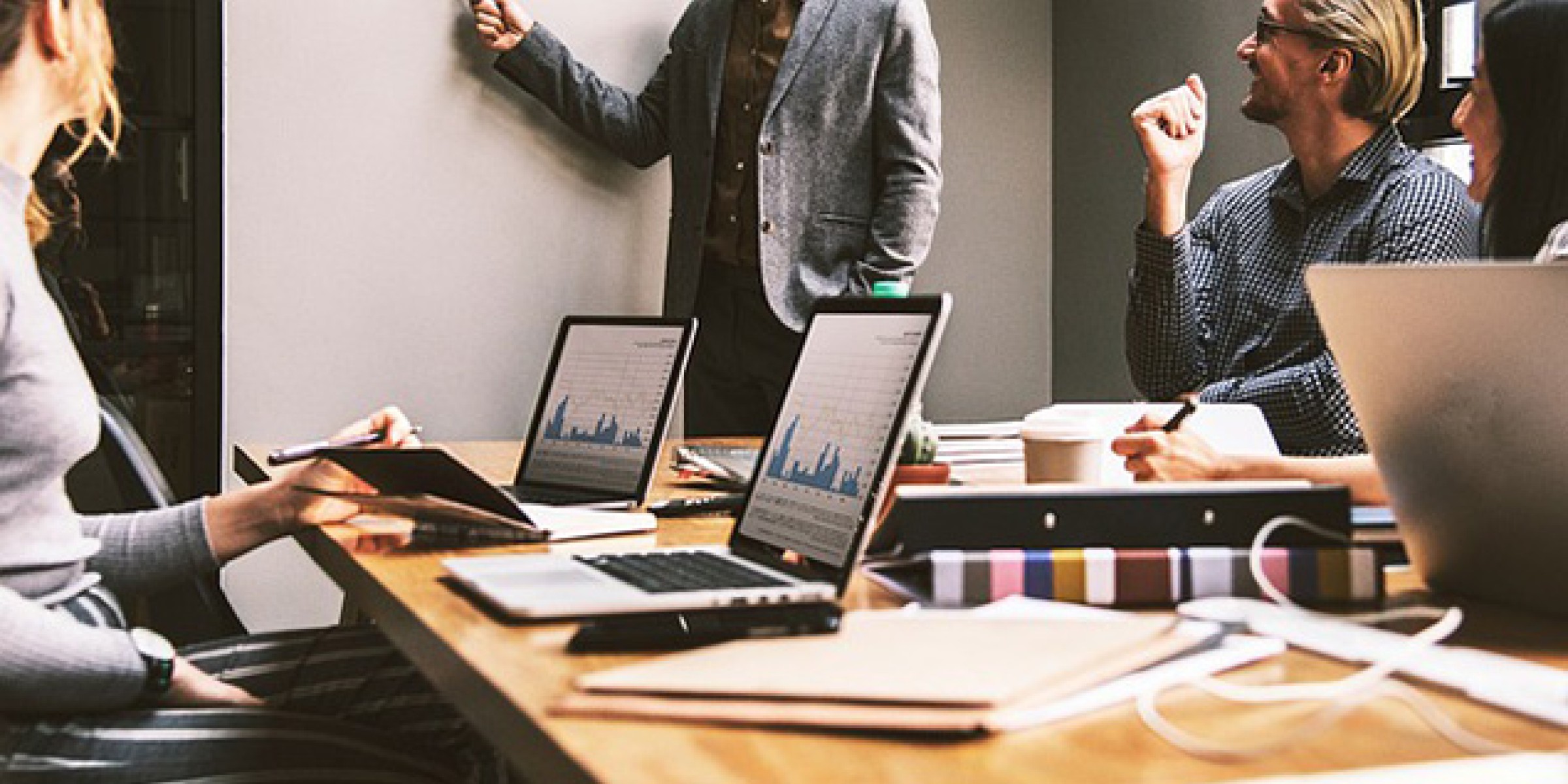 People in a business meeting. There are laptops on a table and a person standing at a white board